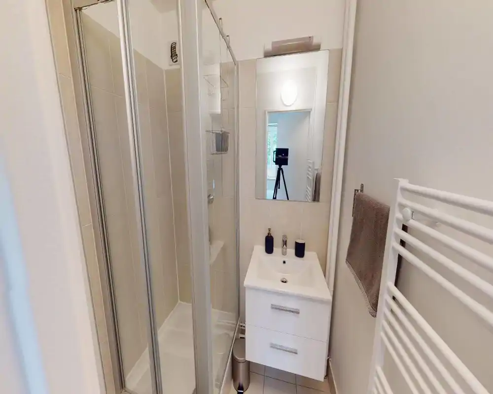 Compact modern bathroom with a tiled shower cabin, wall-mounted vanity with sink and mirror, heated towel rail and neutral decor — bright and clean.