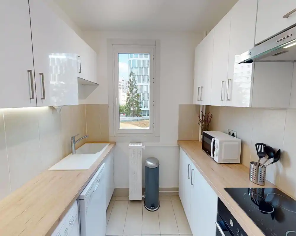 Bright, modern galley kitchen with white cabinets, wood-effect countertops, induction hob and a window providing natural light — neat and functional layout ideal for short-term rentals.
