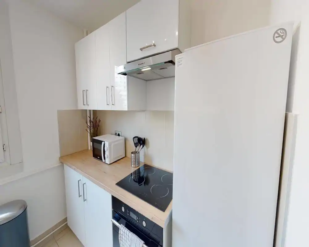 Compact modern kitchen with a glass-ceramic hob, built-in oven and refrigerator. Light wooden countertop, white cabinets and a microwave create a clean, functional cooking area.