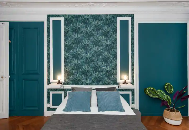 Camera da letto elegante con letto matrimoniale centrale, carta da parati decorativa color teal, lampade da comodino e cuscini coordinati — luminosa, ben arredata e accogliente.