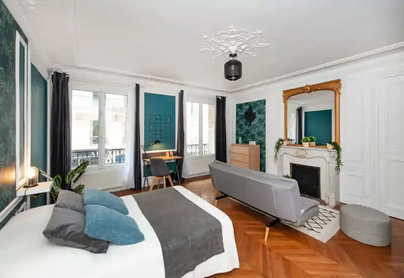 Ampia e elegante camera da letto con letto matrimoniale comodo, grandi finestre che garantiscono molta luce naturale, una scrivania e un'area salotto davanti a un camino e uno specchio decorativi.