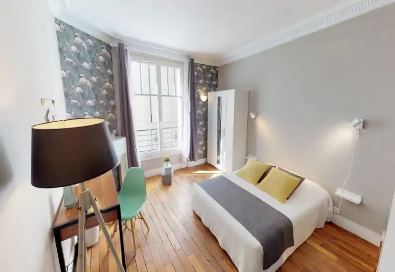 Camera da letto luminosa e di design con letto matrimoniale, carta da parati con fenicotteri, armadio e una grande finestra che illumina l'ambiente.