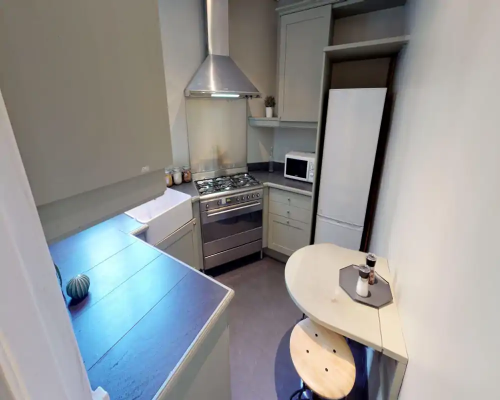 Compact and well-equipped kitchen with a gas range, extractor hood, fridge, microwave and a small breakfast table — neutral cabinetry and tidy countertops make it practical for short stays.
