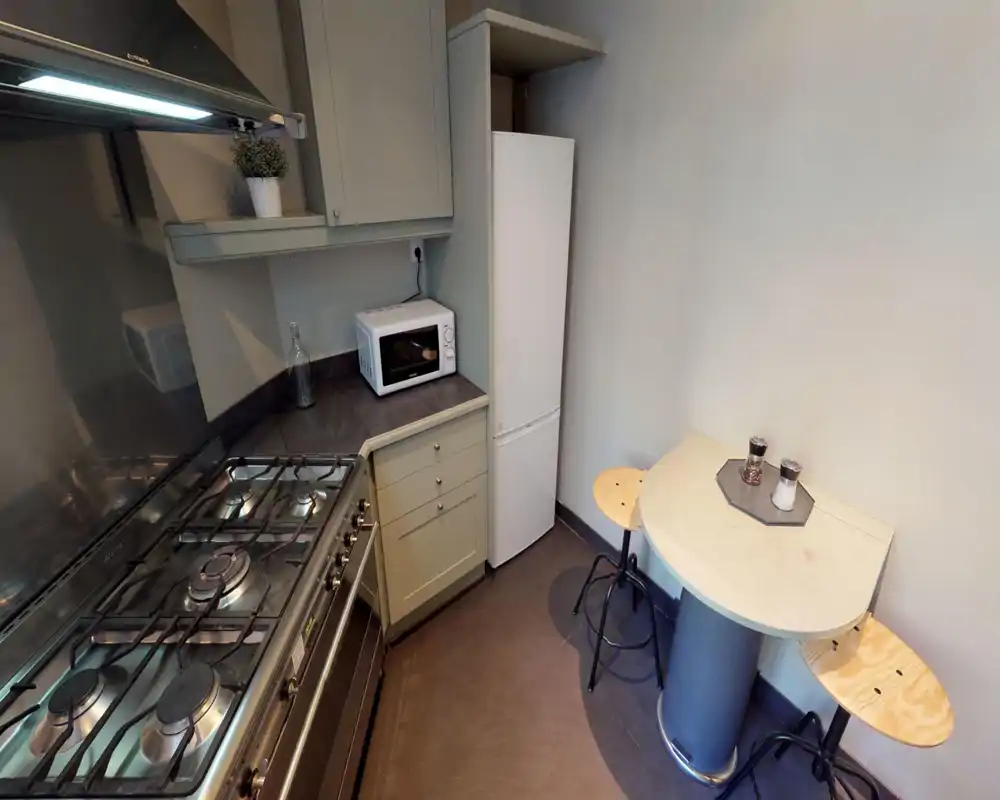 Compact, well-equipped kitchen with a gas hob, oven, fridge and microwave; a small wall table with two stools creates a cozy breakfast corner.