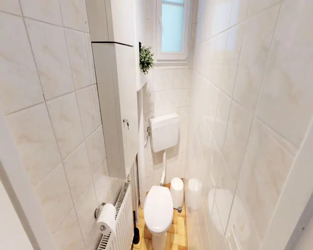 Compact tiled bathroom with a wall-mounted cistern toilet, small window and radiator. Clean, well-lit small WC ideal for a single occupant.