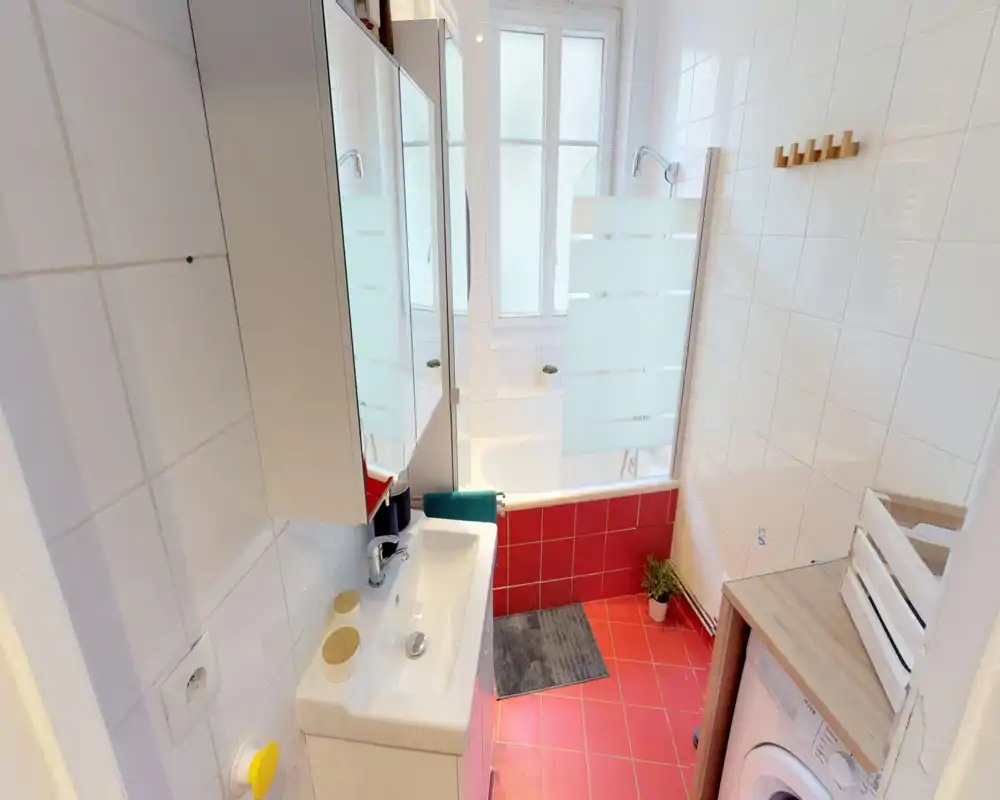 Bright, modern bathroom with a sink, mirror cabinet, bathtub with frosted glass screen and red floor tiles.