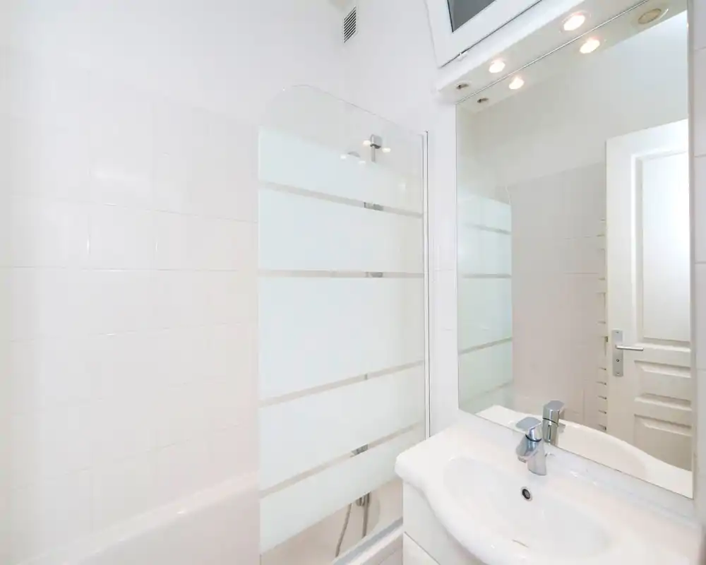 Bright, modern bathroom with white tiles, a sink and mirrored cabinet, and a bathtub with a frosted glass shower screen.