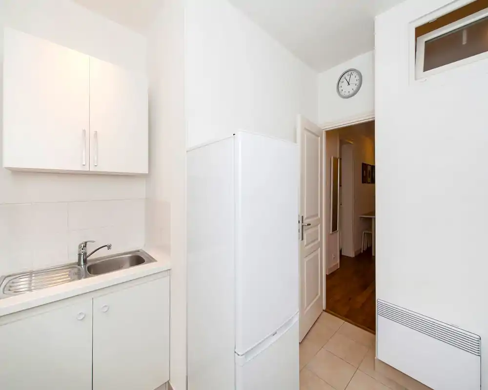 Small, modern kitchenette with a stainless steel sink, white cabinets and a freestanding refrigerator. Bright, clean space suitable for a compact apartment.