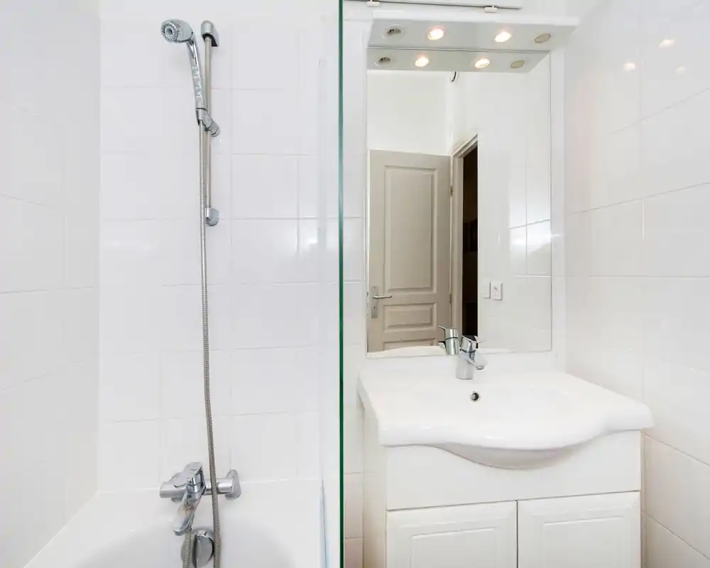 Clean, modern bathroom with white tiles, a bathtub with handheld shower and a sink with mirror and vanity.