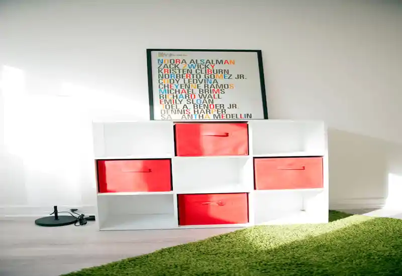 Espace de vie lumineux et minimaliste avec une étagère cube blanche, des boîtes de rangement vertes, une affiche colorée et un tapis vert — style propre et moderne idéal pour une annonce.