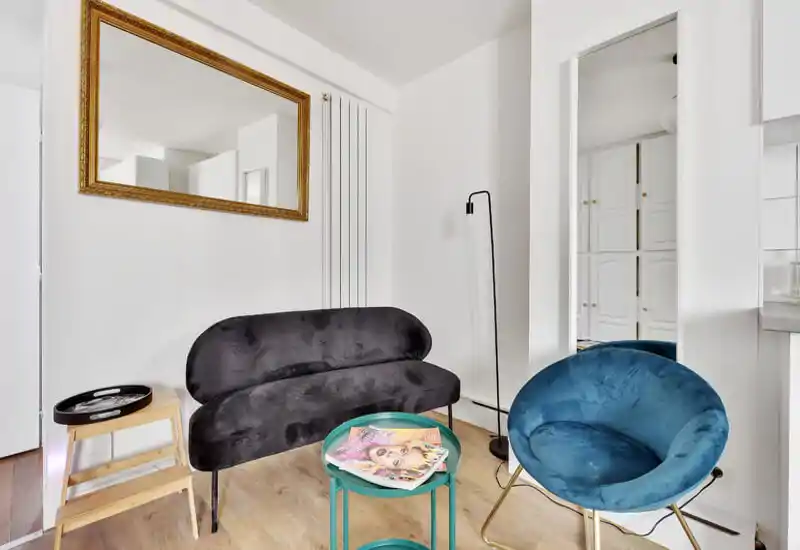 Petit salon stylé avec assises en velours, un fauteuil rond et un canapé compact autour d'une table basse — murs blancs lumineux et décor soigné pour un espace moderne et accueillant.