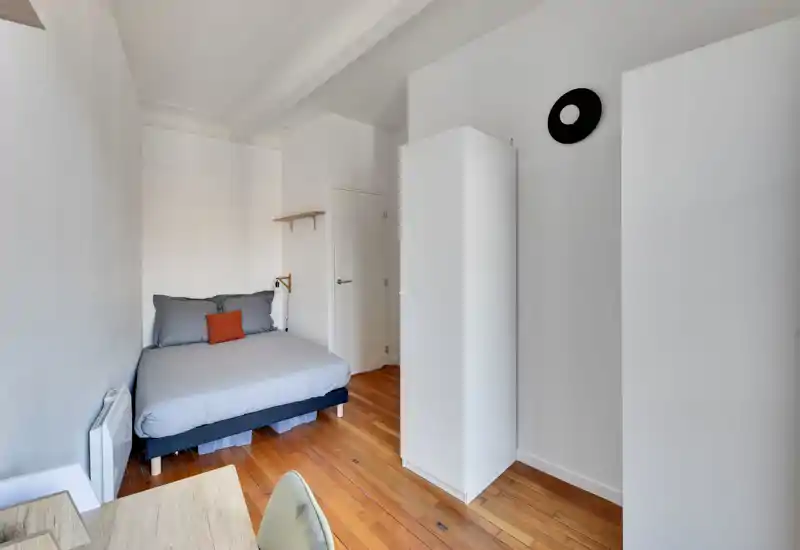 Chambre sobre et lumineuse avec un lit double bien fait, parquet chaleureux et rangement blanc. L'espace est propre et bien éclairé, parfait pour une location courte durée ou un studio.