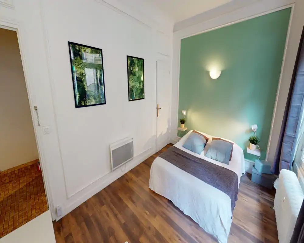 Chambre lumineuse et bien décorée avec un lit double contre un mur vert, étagères de chevet et éclairage doux — idéale pour un séjour confortable.