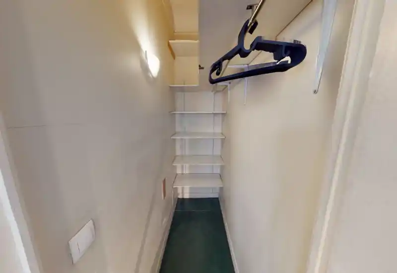 Narrow entry closet with built-in shelving and a clothes rail. Clean but compact storage space ideal for coats and shoes.