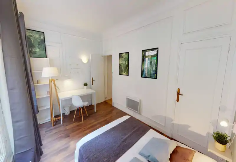 Bright, well-staged bedroom with a comfortable bed, bedside lamp and a small desk area — ideal for relaxing or working. Light wood floors and minimalist décor create a calm, modern atmosphere.
