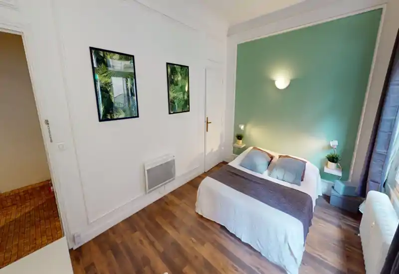Bright, well-styled bedroom with a double bed against a green accent wall, bedside shelves and soft lighting — ideal for a cozy rental stay.