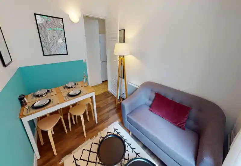 Bright, well-staged living area with a comfortable two-seat sofa, decorative rug and a small dining table set for four — ideal for cozy city stays.