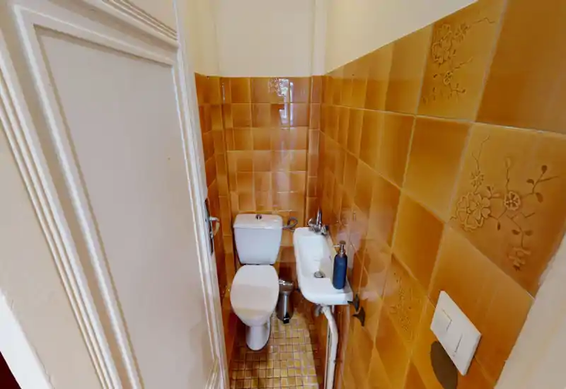 Compact bathroom with white toilet and small wall-mounted sink set against warm ochre decorative tiles; suitable for a guest WC.