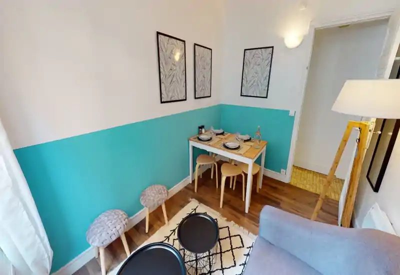Bright, stylish living area with a compact dining corner set against a turquoise half-wall, cozy stools, patterned rug and soft lighting — ideal for a small apartment.