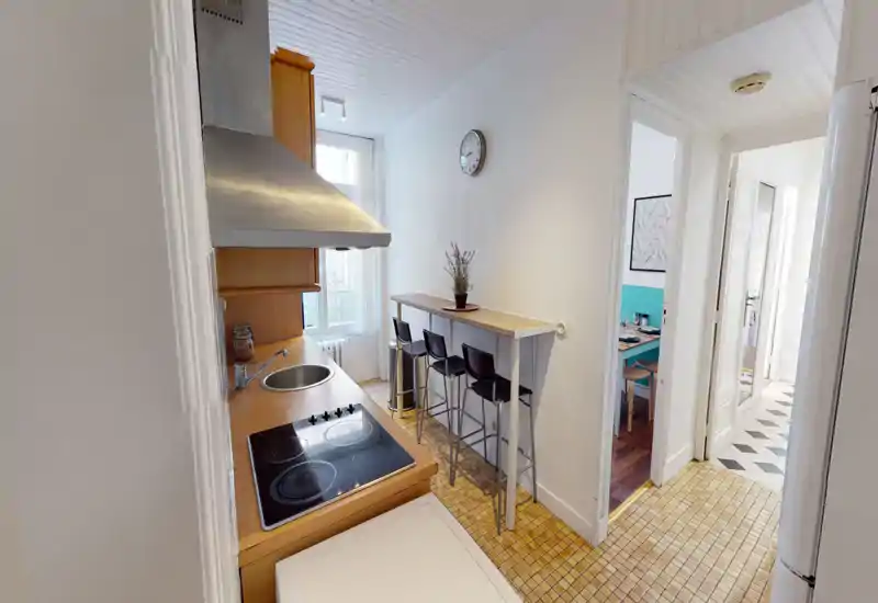 Compact, well-equipped kitchen with a ceramic cooktop, stainless sink, extractor hood and a narrow breakfast bar with stools — bright, tidy and practical for city living.
