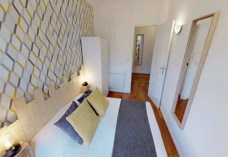 Camera da letto luminosa e di stile con letto matrimoniale, cuscini decorativi e parete con carta da parati geometrica; parquet e lampade da comodino che creano un'atmosfera calda e moderna.