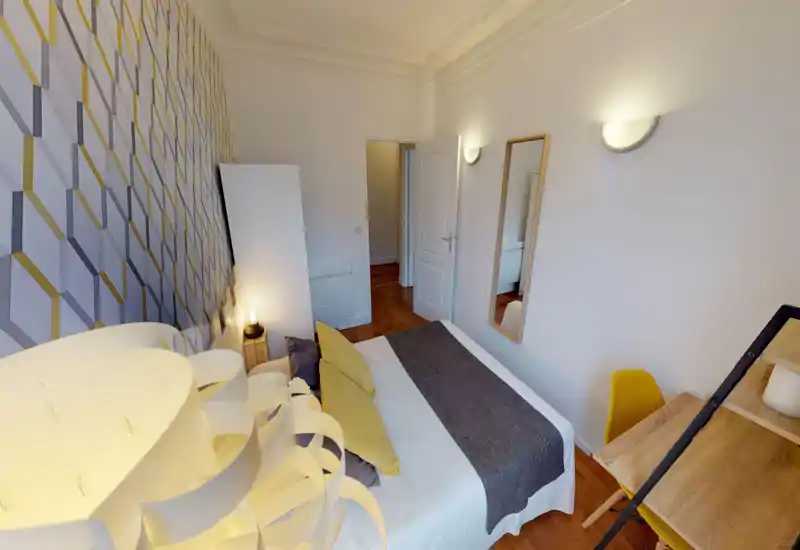 Camera da letto luminosa e di stile con letto matrimoniale ben rifatto, parete decorativa, lampada da comodino e un piccolo angolo scrivania — accogliente e ben arredata.