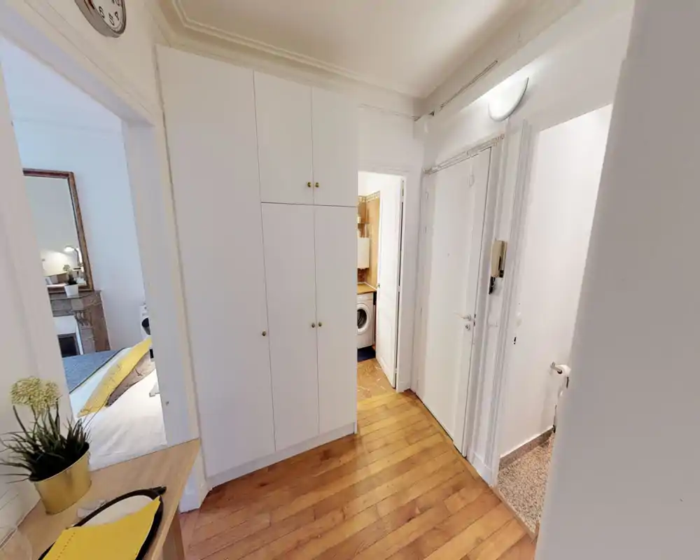 Entrada luminosa y bien presentada con armario empotrado y suelo de madera; se ven puertas hacia el dormitorio, el baño y una pequeña zona de lavandería.