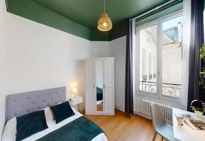Chambre lumineuse et élégante avec un lit double confortable, plaids verts et coussins assortis. Grande fenêtre apportant beaucoup de lumière, armoire, table de chevet avec lampe et un petit bureau — un espace chaleureux et bien agencé pour se détendre ou travailler.