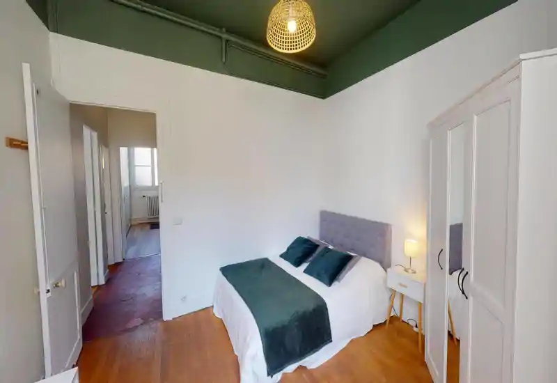 Chambre lumineuse et bien mise en scène avec lit double, tête de lit capitonnée, table de chevet avec lampe et armoire. Le plafond vert apporte du caractère et la pièce bénéficie d'une belle luminosité.