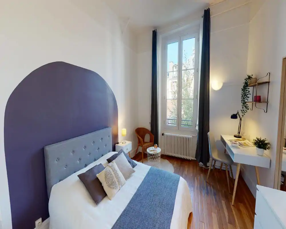 Chambre lumineuse et élégante avec un lit double confortable, une tête de lit peinte, une lampe de chevet et un espace de travail près d'une grande fenêtre. Parquet et textiles doux apportent une ambiance chaleureuse et accueillante, idéale pour une annonce.