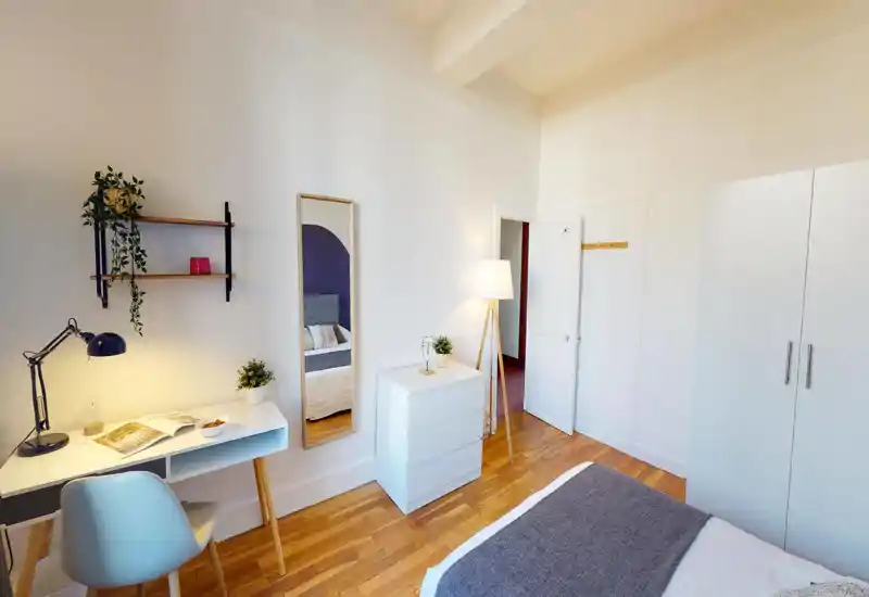 Bright, modern bedroom with a neatly made bed, minimalist desk area and wardrobe. Natural light and warm accents create a welcoming, well-staged space ideal for rental listings.