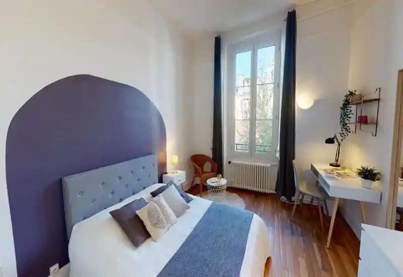 Bright, stylish bedroom with a comfortable double bed, decorative painted headboard, bedside lamp and a workspace by a large window. Wooden floors and soft textiles create a warm, inviting atmosphere ideal for rental listings.