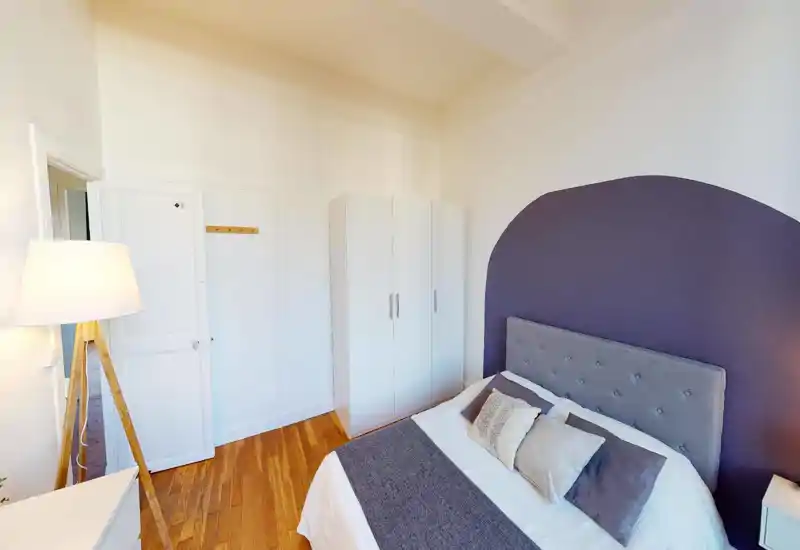 Well-lit and stylish bedroom with a comfortable double bed, tufted headboard and decorative pillows, plus a white wardrobe and warm wooden floors.