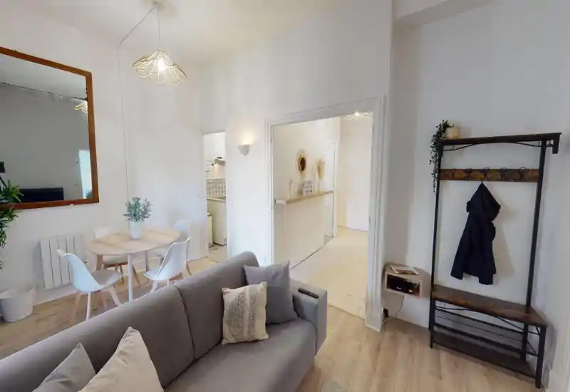 Salon spacieux et élégant avec un canapé gris confortable, coussins, table à manger ronde avec chaises modernes et plantes décoratives, offrant une ambiance chaleureuse et accueillante.