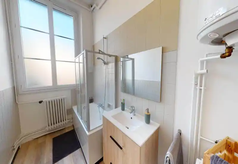 Bright, modern bathroom with a bathtub and glass shower screen, a vanity with sink and mirror, and visible radiator and plumbing.