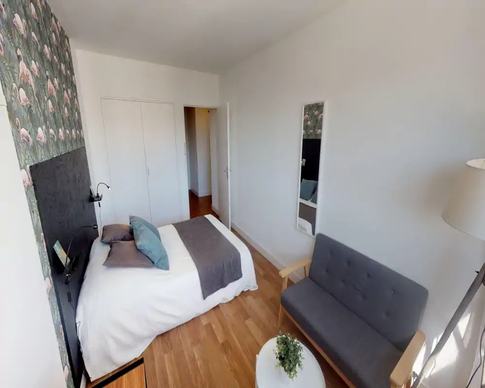 Bright, well-styled bedroom with a double bed, decorative cushions and a cozy throw; a small sofa and lamp create a comfortable seating area.