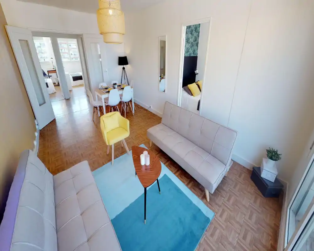 Bright, modern living room with two light sofas, a blue area rug and a small wooden coffee table; dining area and bedroom visible through open double doors, ideal for rental listings highlighting an open-plan layout.
