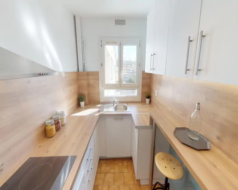 Bright, compact galley kitchen with warm wooden countertops, white cabinets, a sink under the window and modern induction hob — ideal for city apartments.