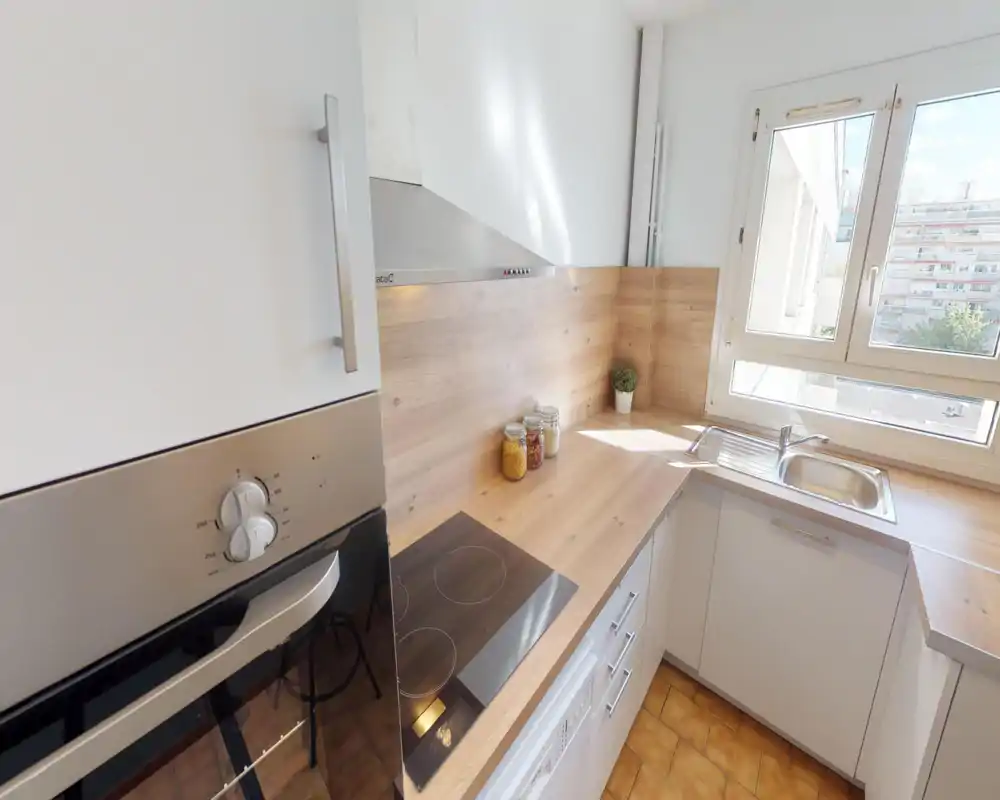 Bright, modern kitchen with wood-effect countertops, electric hob, built-in oven and a sink under a large window letting in plenty of natural light.
