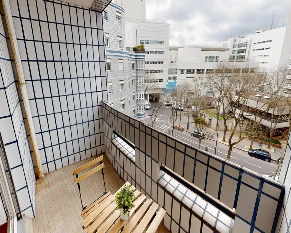 Balcone piastrellato con un piccolo tavolo e sedia in legno e vista sulla strada e sugli edifici vicini — perfetto per un caffè mattutino.