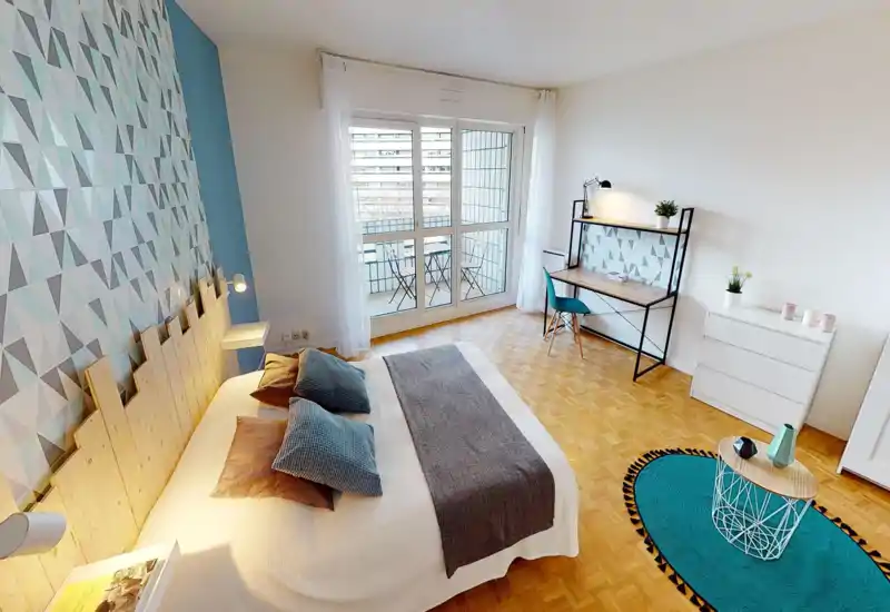 Camera da letto luminosa e moderna con grande letto matrimoniale, parete decorativa a motivo geometrico, scrivania e accesso al balcone. Pavimento in legno e tessili coordinati creano un ambiente accogliente per annunci.