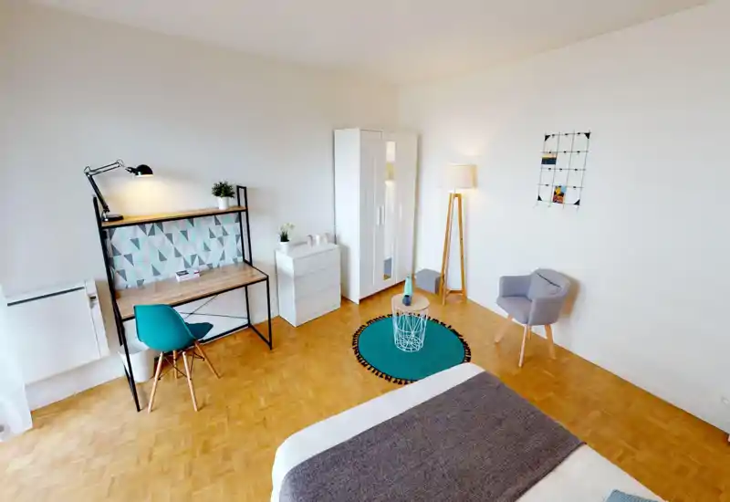 Camera da letto luminosa e di design con letto in primo piano, scrivania con motivo geometrico, armadio e una comoda poltroncina — ideale per un singolo.