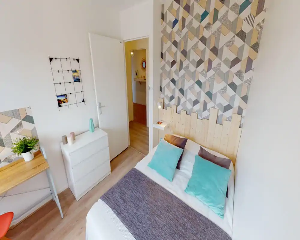 Camera da letto luminosa e ben arredata con letto matrimoniale, parete decorativa a motivi e cuscini coordinati — perfetta per un soggiorno confortevole.