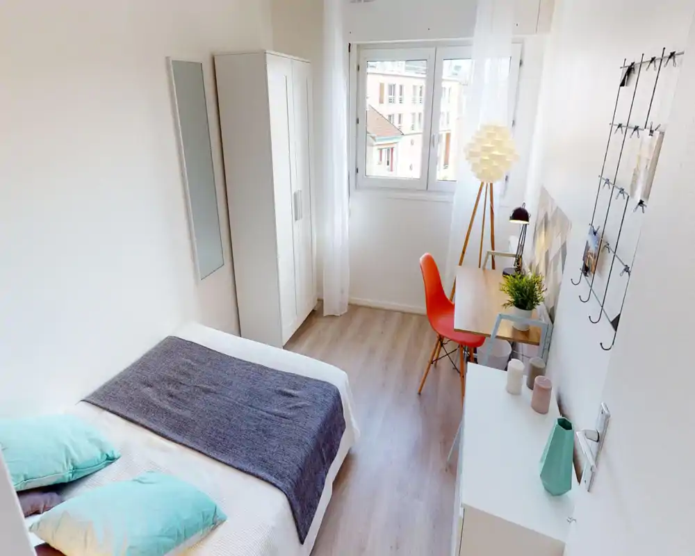 Camera da letto singola moderna e luminosa con letto rifatto, armadio, scrivania e finestra che garantisce molta luce naturale — ideale per uno studente o single.