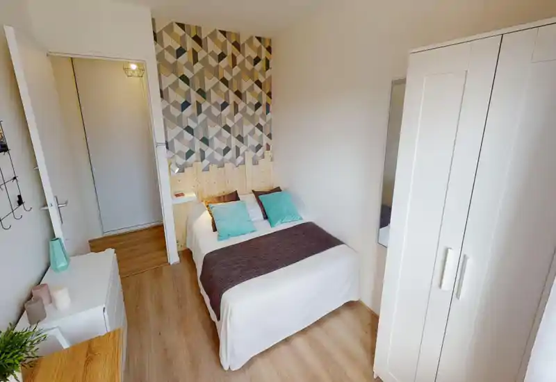 Camera da letto ben allestita con letto matrimoniale, parete decorativa a motivi e pavimento in legno chiaro; luminosa, ordinata e accogliente per affitti brevi.