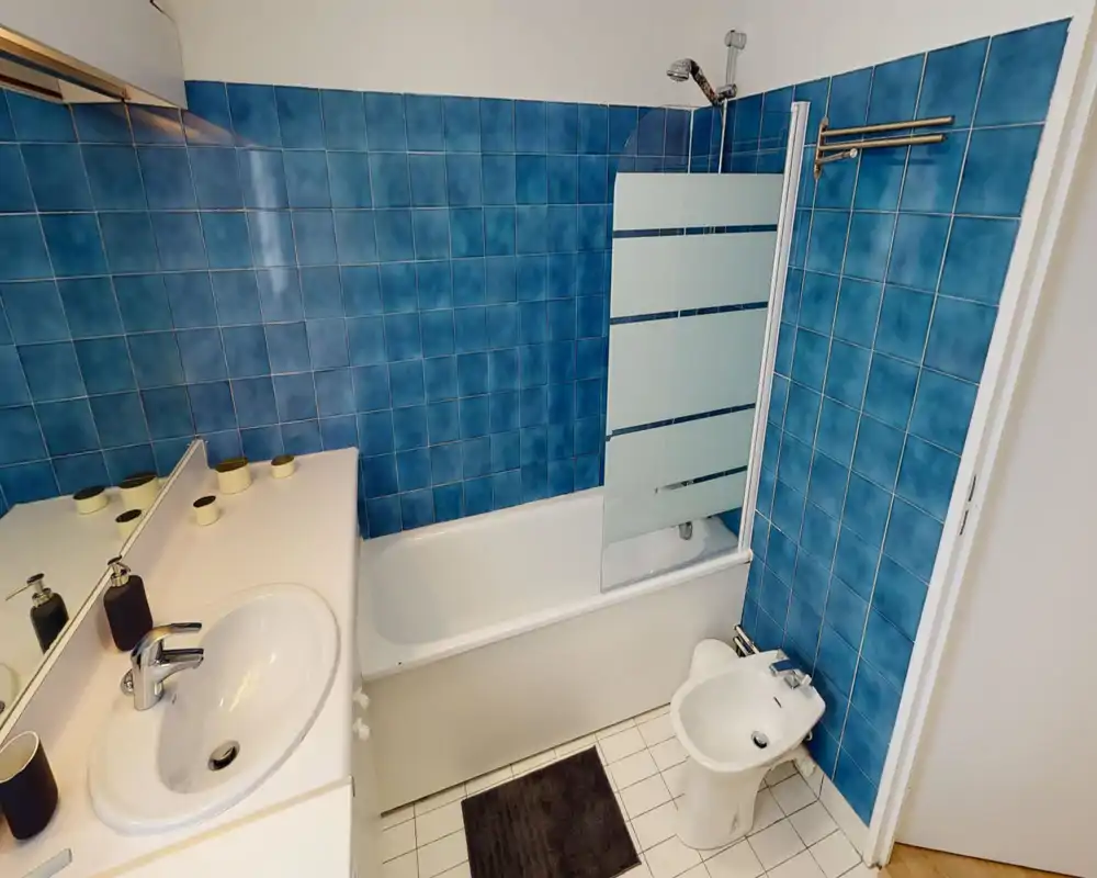 Bagno pulito e ben illuminato con vasca/doccia, pareti piastrellate blu, lavabo e bidet — spazio pratico e ordinato per gli ospiti.