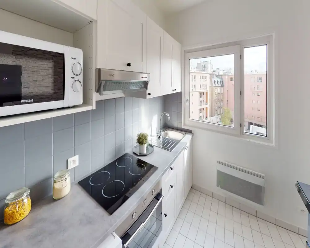 Cucina compatta e luminosa con piano cottura elettrico, forno e microonde incassati, mobili chiari e una finestra che offre luce naturale.