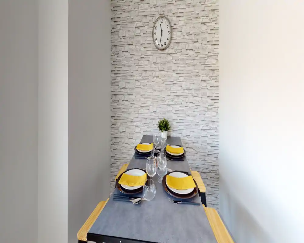Angolo pranzo moderno e luminoso con tavola apparecchiata per quattro, parete effetto pietra e una piccola pianta decorativa — perfetto per mostrare mise en place.