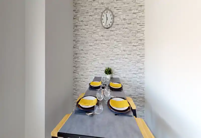 Angolo pranzo moderno e luminoso con tavola apparecchiata per quattro, parete effetto pietra e una piccola pianta decorativa — perfetto per mostrare mise en place.