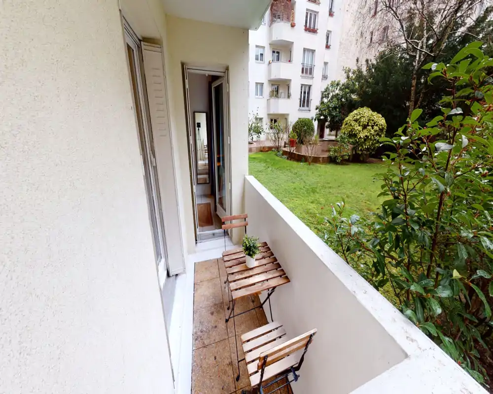 Balcón pequeño y acogedor con mesa bistró y dos sillas con vistas a un jardín comunitario verde — ideal para el café matutino.